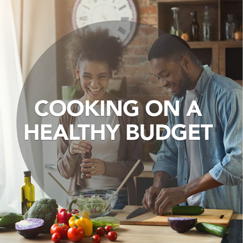 Multi racial couple cooking a healthy dinner. They are chopping fresh veggies, like broccoli, red onion, red, green and yellow peppers, tomatoes, lettuce, spinach, cucumbers, olive oil and spices (black pepper, salt). Couple is laughing & enjoying company